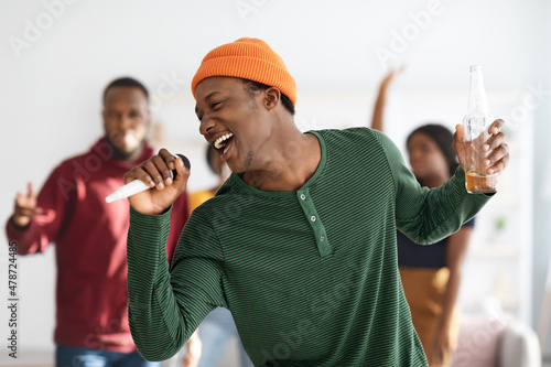 Joyful african american man with bottle of beer singing karaoke