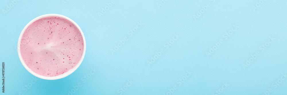 White paper cup of berry ice cream on light blue table background. Pastel color. Closeup. Wide banner. Cold sweet snack in summer. Empty place for text. Top down view. White paper cup of berry ice cream on light blue table background. Pastel color. Closeup. Wide banner. Cold sweet snack in summer. Empty place for text. Top down view.