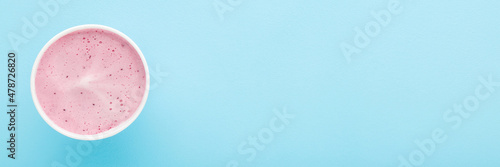 White paper cup of berry ice cream on light blue table background. Pastel color. Closeup. Wide banner. Cold sweet snack in summer. Empty place for text. Top down view.