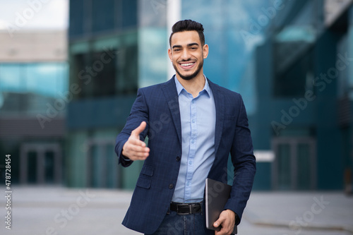 Positive arab man in formal suit outstretching hand towards camera © Prostock-studio