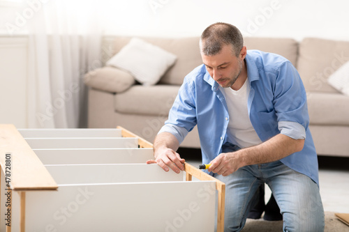 Middle-Aged Male Installing Wooden Cabinet Using Screwdriver At Home