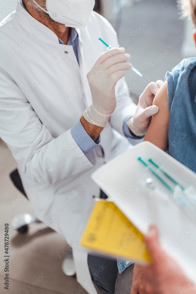 Doctor with face mask injecting antibody to boy in arms at center Doctor with face mask injecting antibody to boy in arms at center