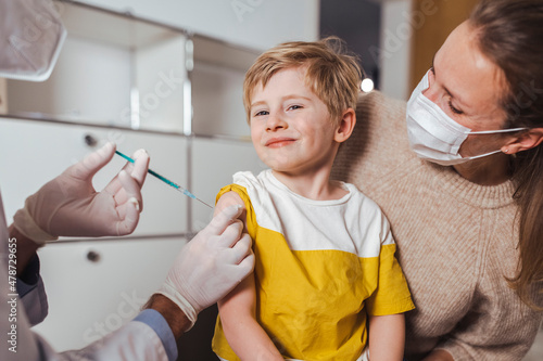 Smiling boy getting vaccine injection by doctor in center photo