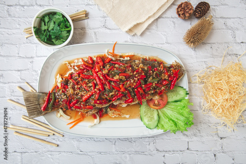 snapper cooked thai style with red hot chilli peppers sauce and cucumbers on a white brick background