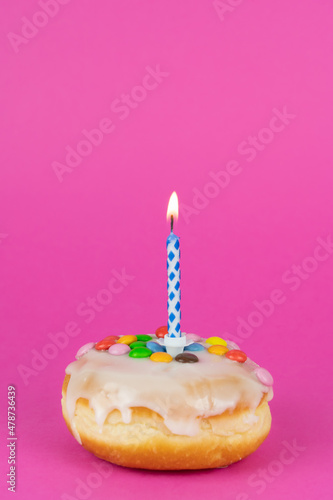 Delicious birthday cake with a burning candle, pink background with copy space