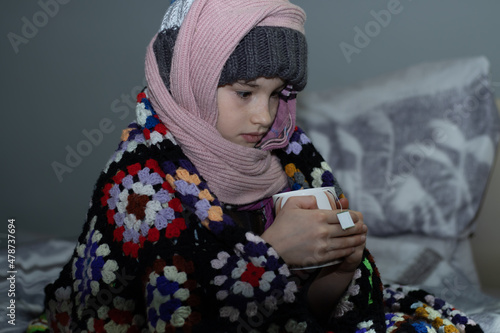 person in warm clothes sitting on a bed with cup of tea