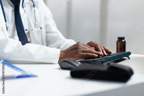 Closeup of african american therapist doctor typing medicine pharmaceutical on computer working at healthcare treatment in hospital office. Man analyzing disease expertise monitoring symptoms