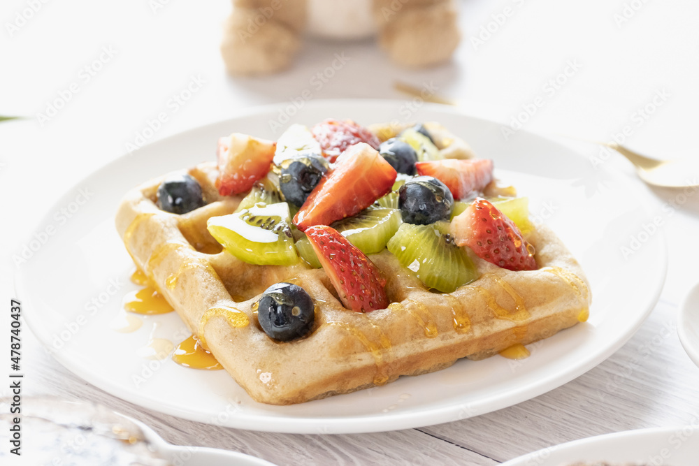 Belgian waffles with fruits berries and honey maple syrup set on white cafe table.
