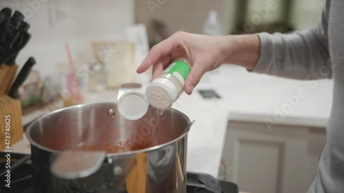 A person hand sprinking some seasoning inside a pot on a stove in slow motion, close up static photo