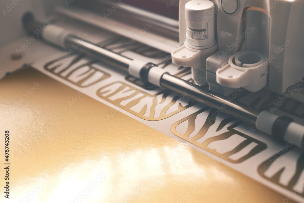 inside view of foil plotting machine while cutting 2022 tiger design stickers from golden vinyl. preperation for chinese new year concept. moody light. selective focus inside view of foil plotting machine while cutting 2022 tiger design stickers from golden vinyl. preperation for chinese new year concept. moody light. selective focus
