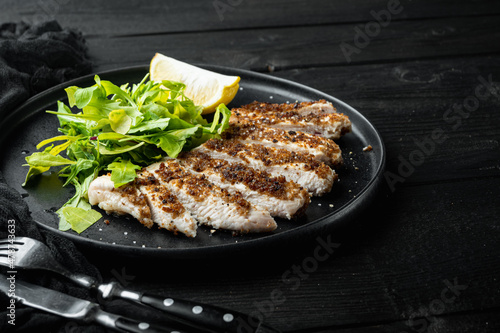 Crumbed chicken breast fillet grilled, over black wooden table with space for text