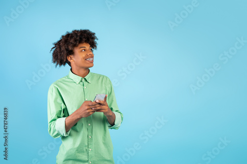 Mobile offer. Happy african american teen guy holding smartphone and looking aside at free space on blue background