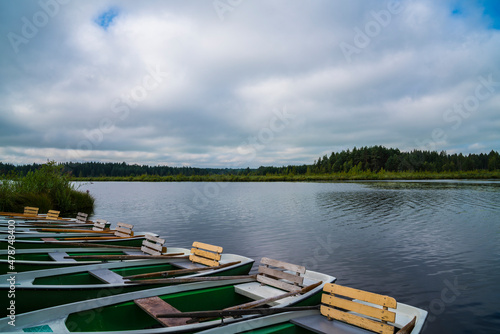 Green rowing boats at lakeshore at a boat rental station ready for sports on a small lake between green forest nature landscape