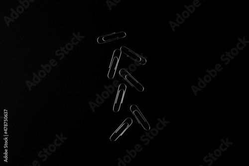 Metal paper clips lie on a black background