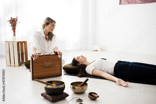 A yoga teacher gives a woman a sound bath lying on the mat. She plays a shruti box from India and there are several Tibetan bowls too