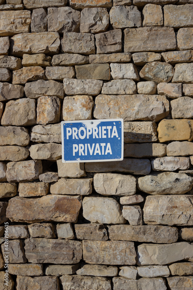 Rustic stone wall with a blue sign with white writing in Italian: Rustic stone wall with a blue sign with white writing in Italian: