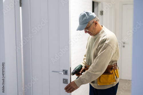Attractive builder is installing lock in door. He is holding a screwdriver and kneeling.