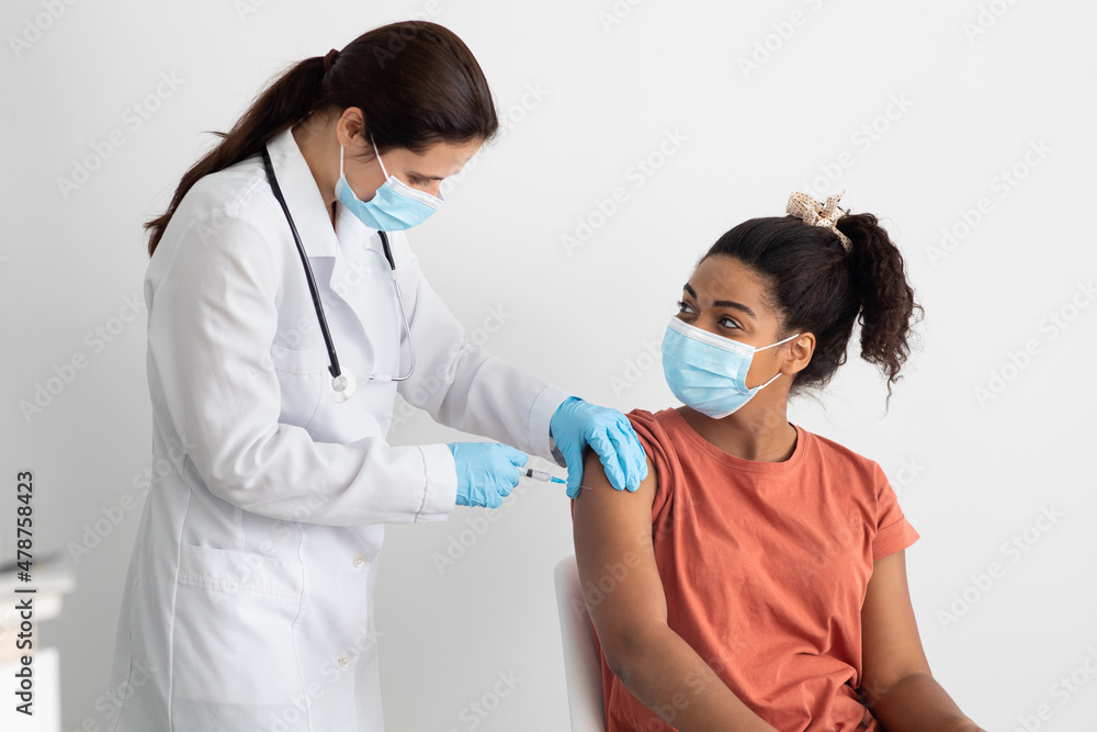 Nurse in white workwear making vaccination for black lady Nurse in white workwear making vaccination for black lady