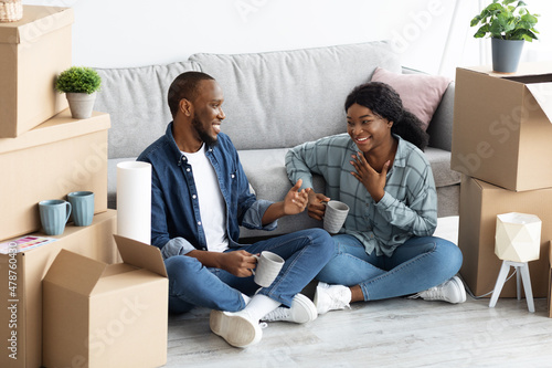 Cheerful Black Spouses Sitting Among Unpacked Cardboard Boxes And Drinking Coffee