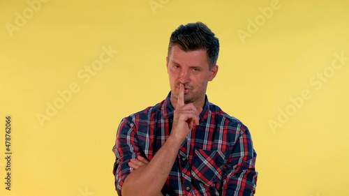 Close up of young man making a hush gesture on yellow background. It must be quite there. photo