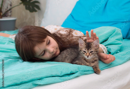 happy girl hugs her kitten. A cute little girl is resting on the bed with her kitten. The concept of pets, childhood.Selective focus.