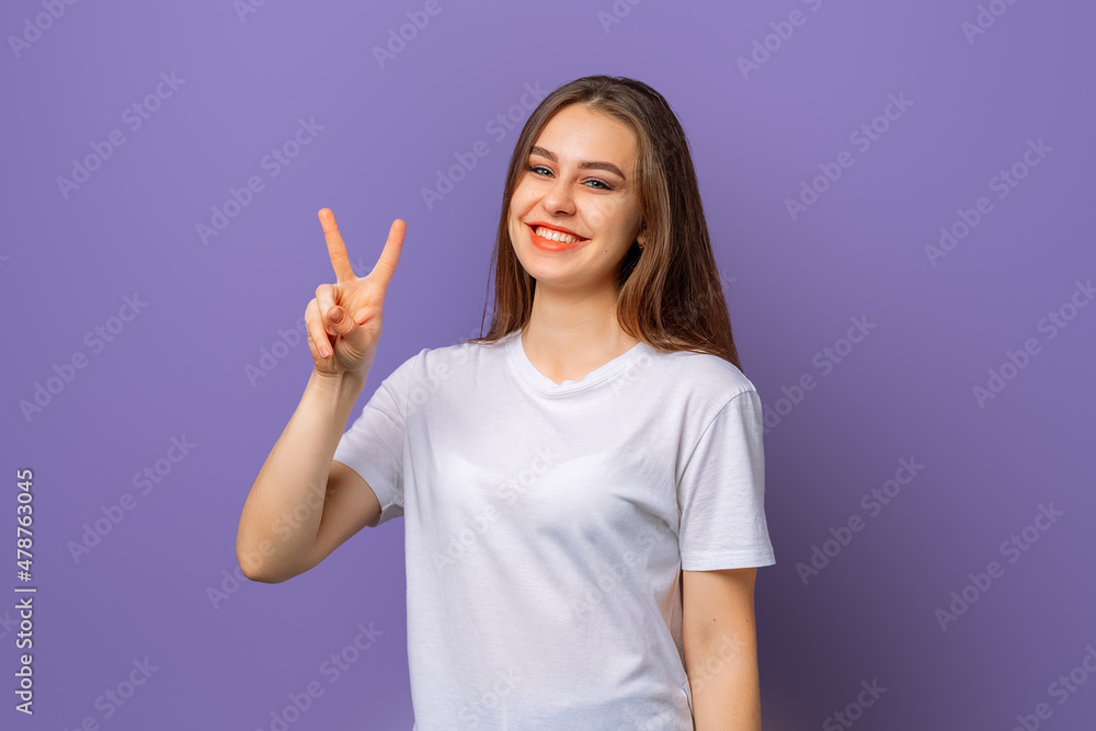 Photo of funny adorable young woman hand fingers show v-sign symbol, peace gesture, with a happy smile on face, standing over magenta color background