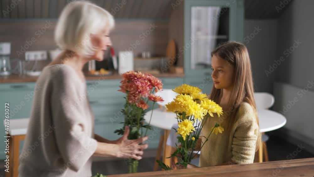 Handsome girl helps to her grandmother collect a bouquet of flowers at home Handsome girl helps to her grandmother collect a bouquet of flowers at home