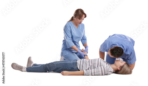 Medical workers in uniform performing first aid on unconscious woman against white background