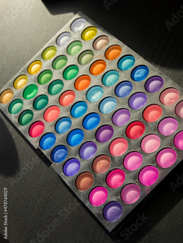 top view of eye shadow and blush palettes near face powder, cosmetic brushes, lipsticks and face foundation on pink