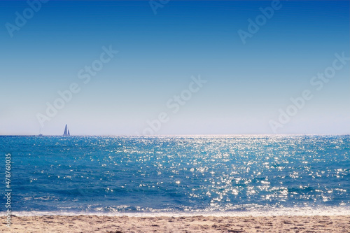 The sky blue seaside in summer. There is a small sailing boat passing by in the distance of the sea horizon. Golden sands.