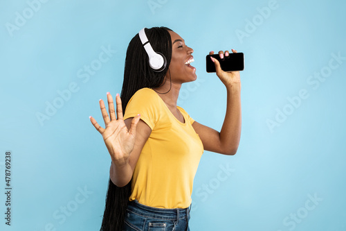 African American Lady Singing Holding Phone Near Mouth, Blue Background photo