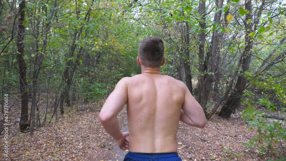 Young muscular man running along trail at early autumn forest. Unrecognizable sportsman sprinting along path at nature. Athletic guy exercising outdoor. Concept of healthy active lifestyle. Rear view Young muscular man running along trail at early autumn forest. Unrecognizable sportsman sprinting along path at nature. Athletic guy exercising outdoor. Concept of healthy active lifestyle. Rear view