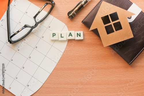 PLAN letterings on white cubes on the calendar. A house model on the notebook  pen  and eyeglasses. Business and plan concept