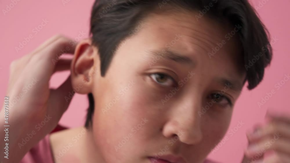 Asian man correcting his appearance at the camera in the pink studio Asian man correcting his appearance at the camera in the pink studio