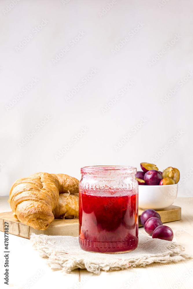 Plum jam in a glass jar. Plum jam, croissants and ripe plums in the background. Plum jam in a glass jar. Plum jam, croissants and ripe plums in the background.