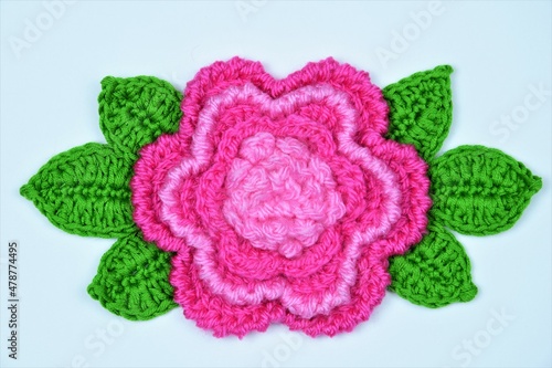 Crocheted flower and leaves on a white paper background
