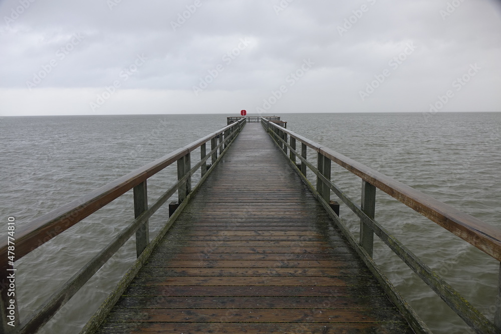 Wooden pier leading into the North Sea during high tide on a rainy day (horizontal image), Burhave, Lower Saxony, Germany