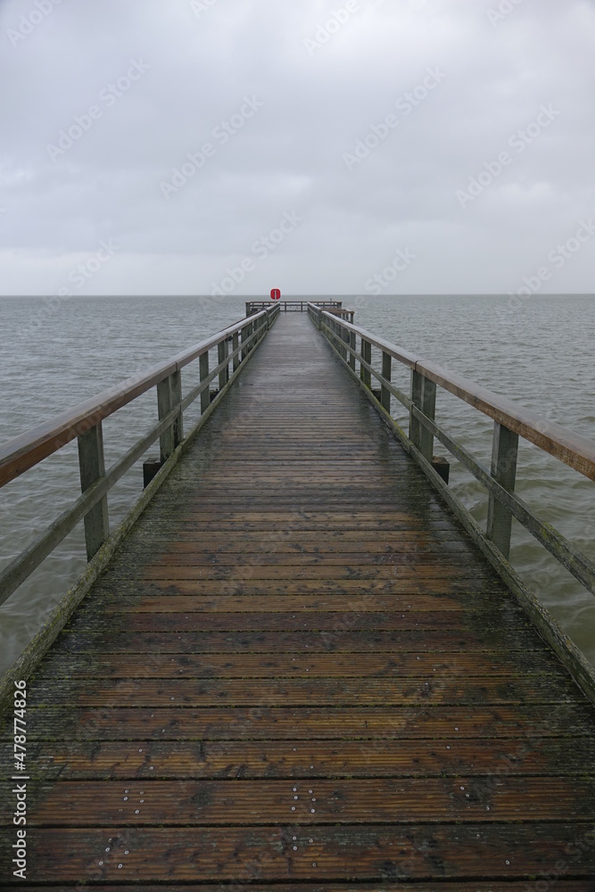 Wooden pier leading into the North Sea during high tide on a rainy day (vertical image), Burhave, Lower Saxony, Germany