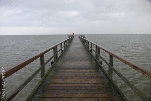 Wooden pier leading into the North Sea during high tide on a rainy day (horizontal image), Burhave, Lower Saxony, Germany