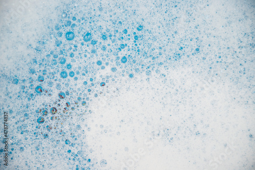 Abstract background texture of white soap foam. Shampoo foam with bubbles on a blue background.