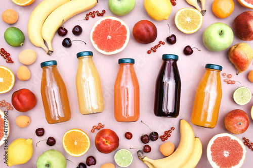 Fresh organic colorful juice in bottles on ripe fruits from market background: apple and orange, grapefruit and banana, grape and berries