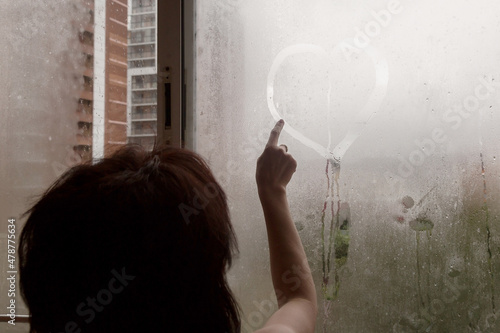 фотографія A woman draws heart with her finger on a wet fogged window