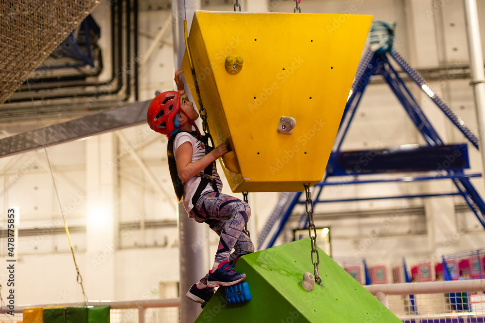 Girl wearing in harness and safety equipment climbing on practical wall