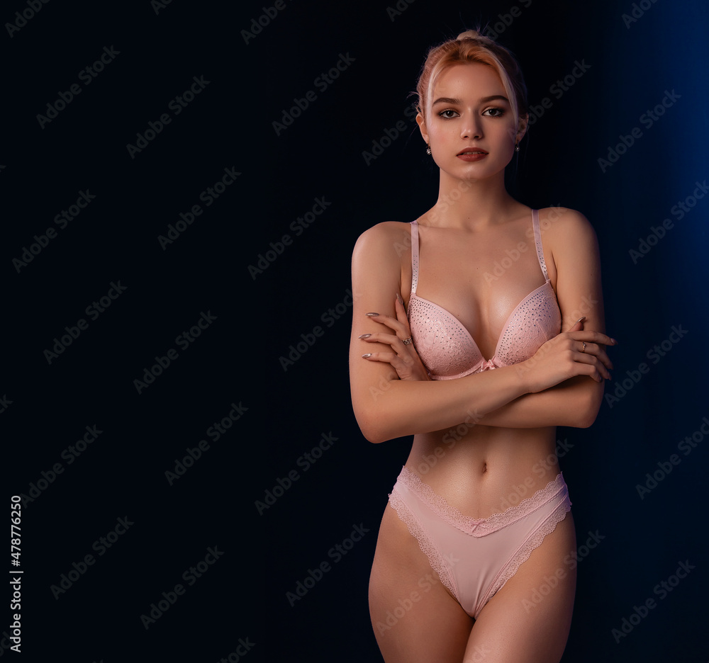 Fototapeta premium Gorgeous woman posing in seductive pink lingerie. Attractive seduce beauty lady. Advertising underwear sensual slim fit body on dark blue background free space for text