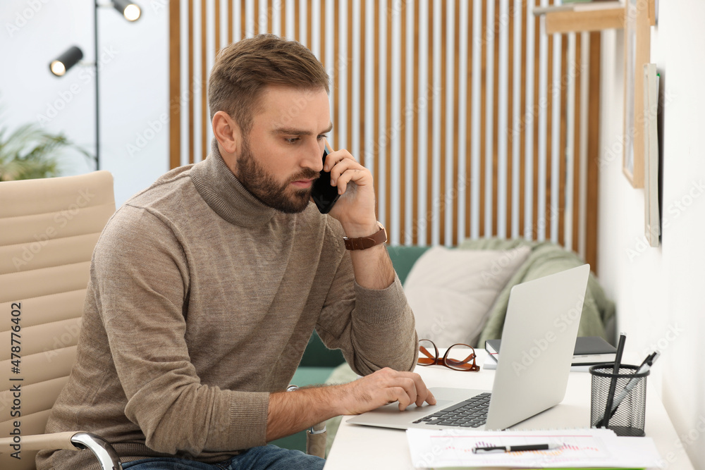 Young man talking on phone while working with laptop at home Young man talking on phone while working with laptop at home