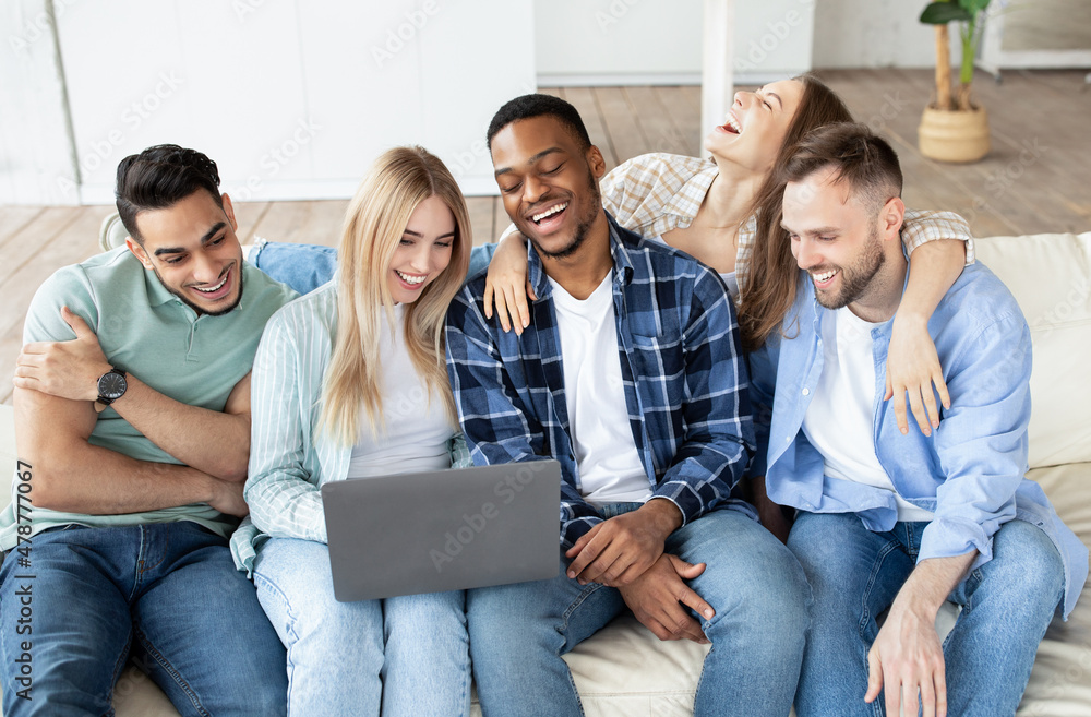 Happy multiethnic friends using laptop computer, sitting on couch, watching movie, having video call from home Happy multiethnic friends using laptop computer, sitting on couch, watching movie, having video call from home