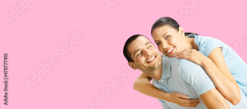 Happy amazed smiling couple. Portrait of standing close embracing, piggyback pose pair in love studio concept, on rose pink color background. Brunette man and woman together. Copy space area.