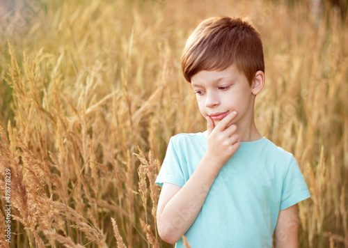 Cute boy stands lost in thought in a field with spikelets