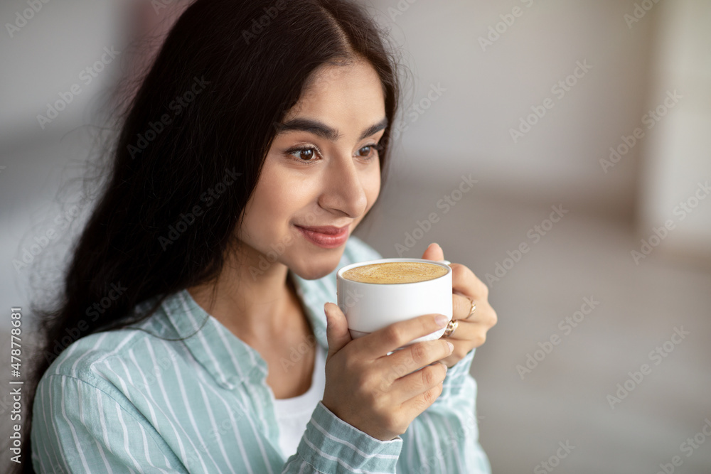 Young Indian woman having coffee break, drinking frothy cappuccino at home, copy space Young Indian woman having coffee break, drinking frothy cappuccino at home, copy space