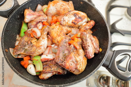 Tasty chicken meat portions in the pan. Frying or roasting processing. Preparing food on a kitchen stove. The classic French delightful dish «Coq au vin». Food background. 